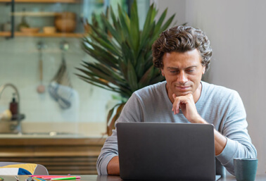 Man with head resting on his hand looking at a laptop