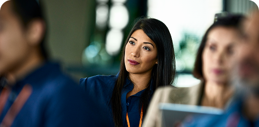 Woman attentively listening at a seminar, with others in the background.
